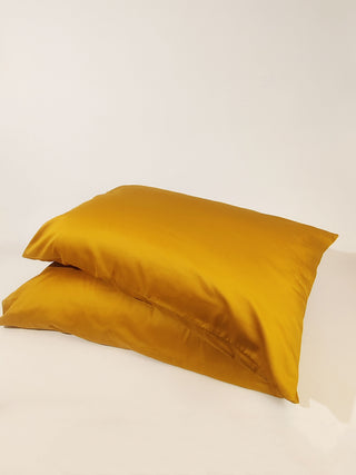 Two pillows with mustard yellow satin-weave pillowcases in organic cotton