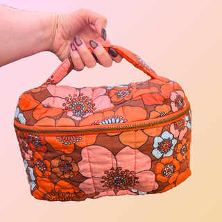 Floral-patterned fabric bag held by a hand on a light pink background
