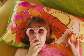 Woman wearing a green top and beige bloomers lying on a colourful silk pillow with a peach