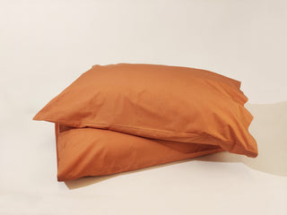 Two pillows with percale rust coloured pillow cases in organic cotton
