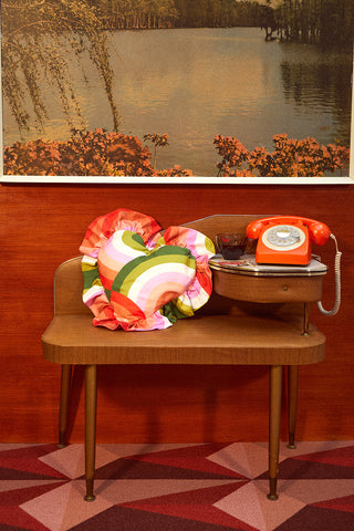 Retro colourful heart shape frilly cushion on vintage telephone table and seat with pattened carpet
