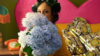 Person holding flowers in a colorful room with a bed and decor.