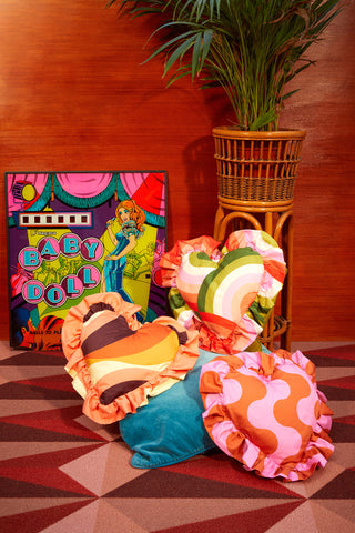 3 heart-shaped cushions in various retro colourful prints in a styled vintage hotel setting with patterned carpet
